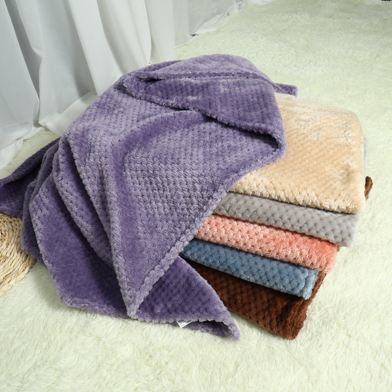 Stack of folded textured blankets in various colors on a light surface.