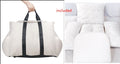 White duffel bag with black straps held by a hand, next to a folded white blanket on a chair.