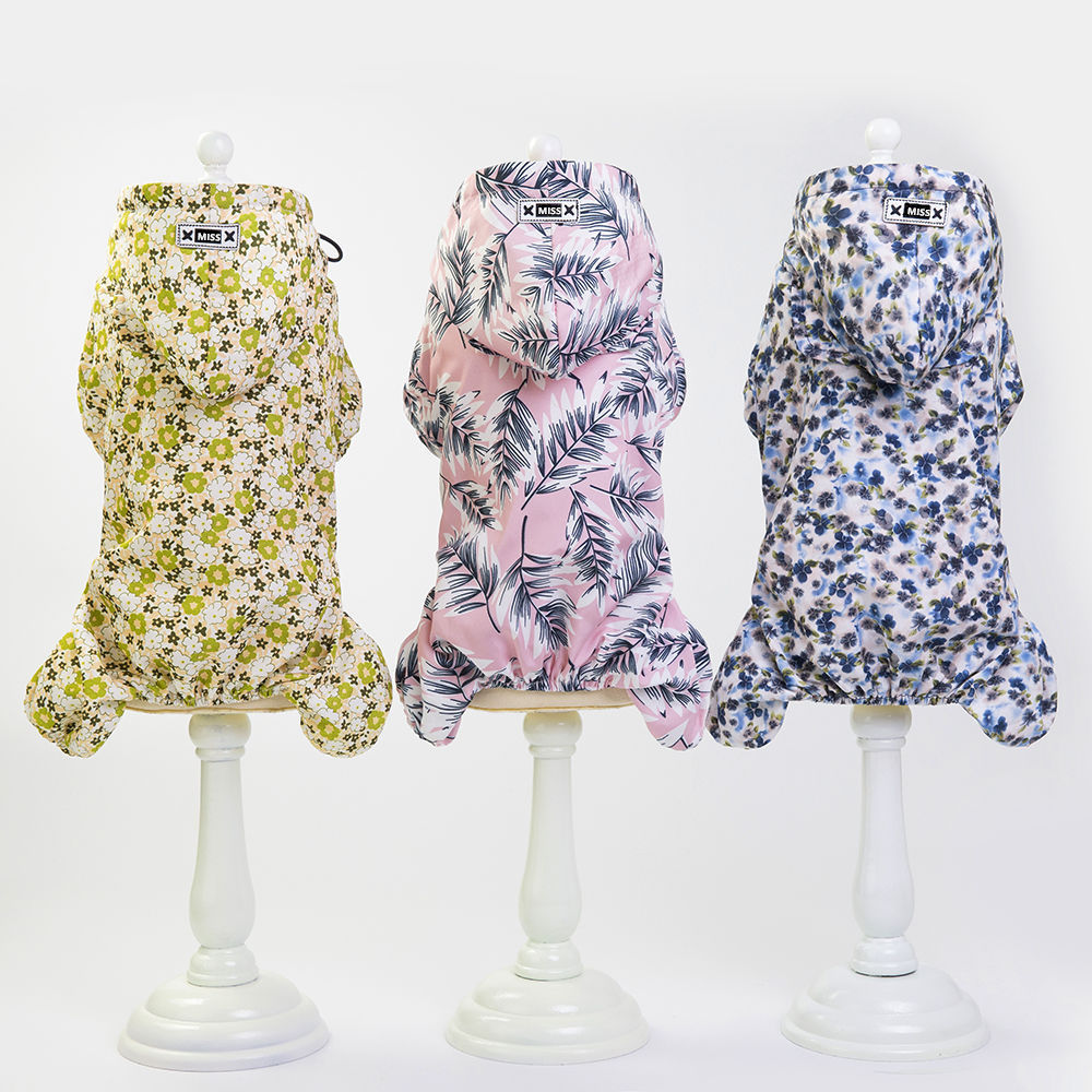 Three hooded dog jackets with floral and botanical prints displayed on white pedestal stands.