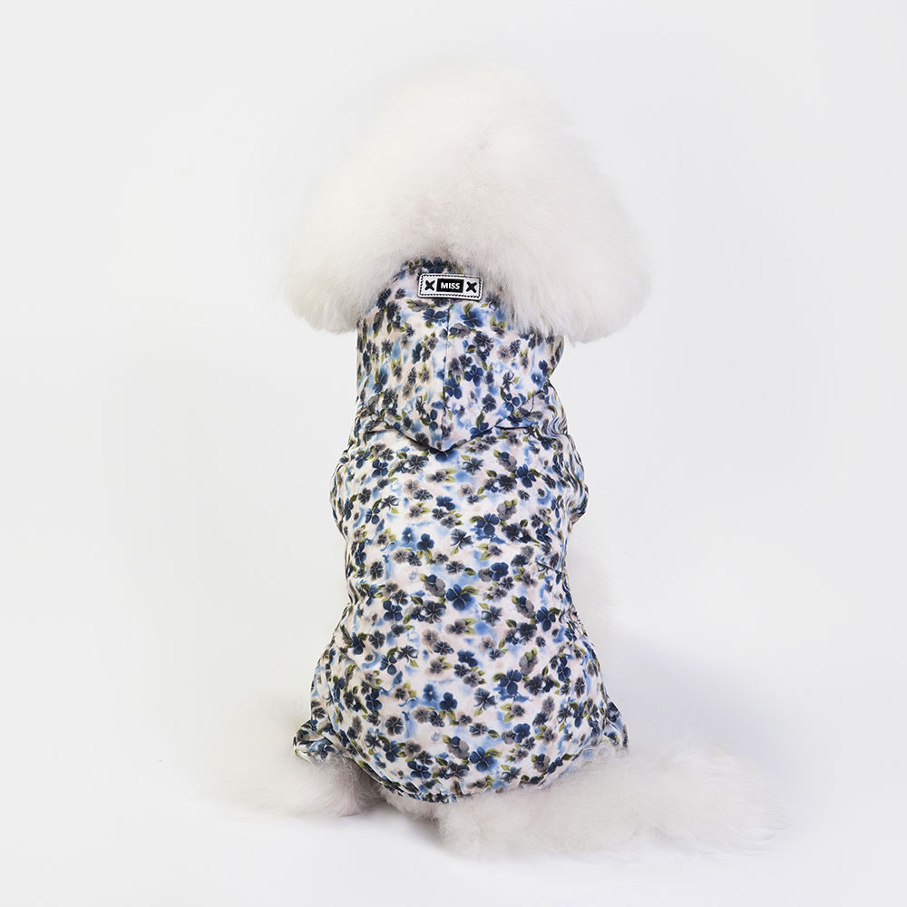 White fluffy dog wearing a blue floral hooded jacket with white fur trim, sitting with its back to the camera.