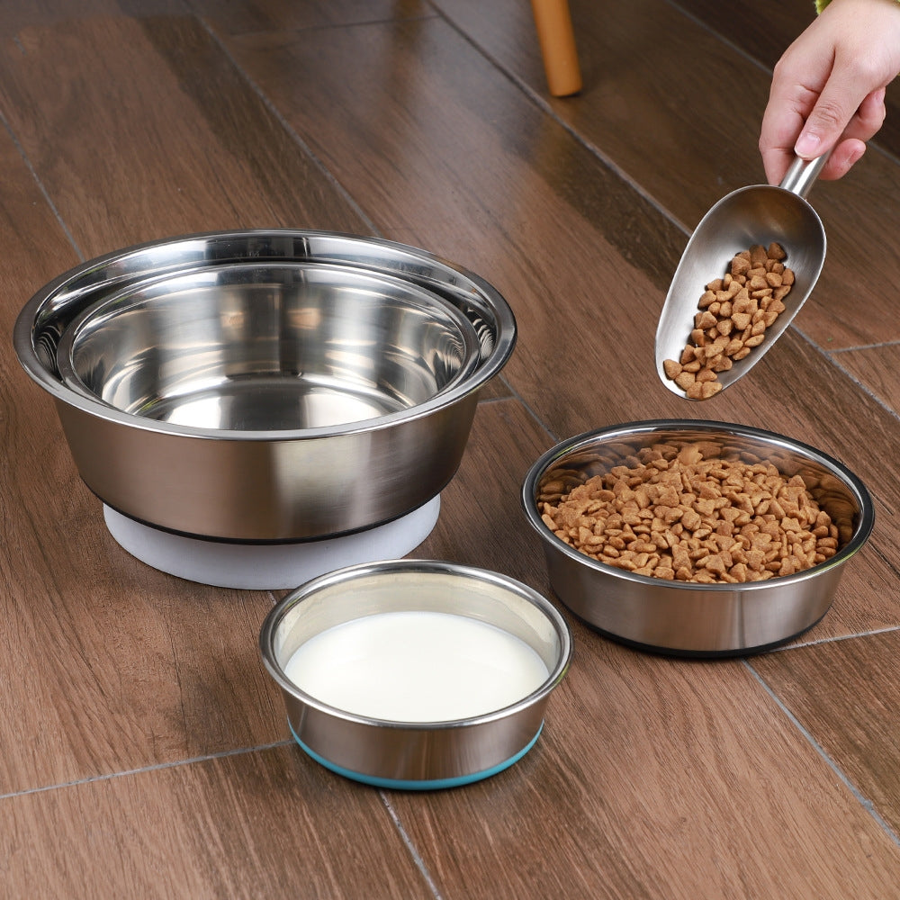 Set of stainless steel pet bowls on a wooden floor with a hand pouring food into one of the bowls.