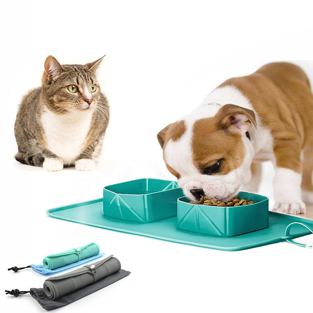 Cat and puppy beside a green silicone pet feeding set with two bowls on a matching mat, with rolled travel mats below.