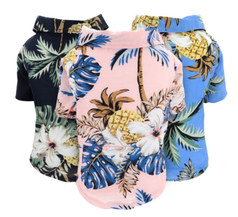 Three tropical pet shirts in blue, pink, and navy with floral and pineapple prints laid side by side.