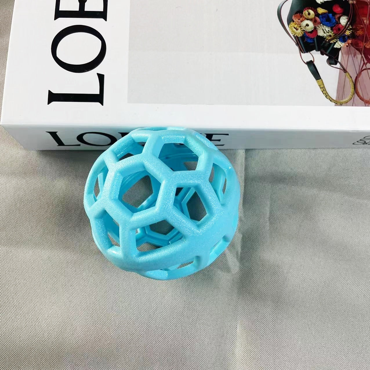 Light blue hollow geometric dog chew ball placed on a grey fabric background.