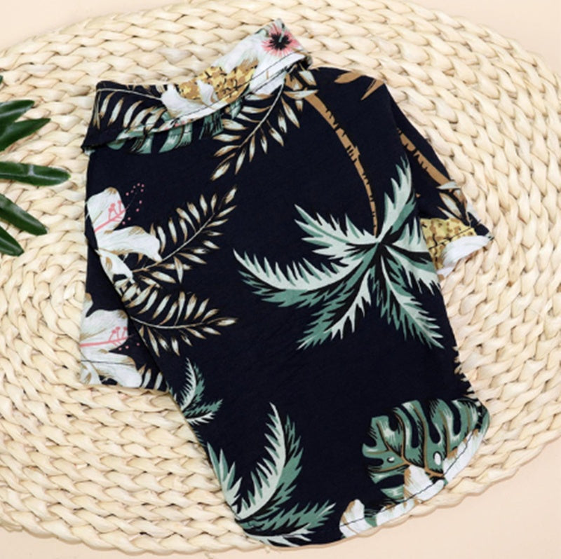 Dark tropical pet shirt with green palm leaves and white flowers laid flat on a woven mat