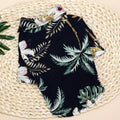 Dark tropical pet shirt with green palm leaves and white flowers laid flat on a woven mat