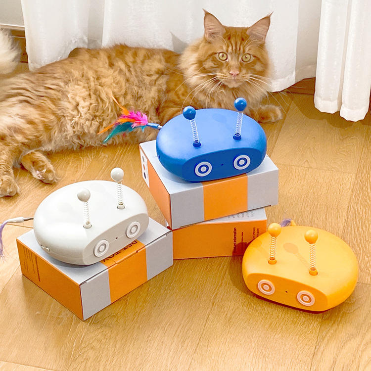 Three colorful cat toys on boxes with a cat sitting in the background.